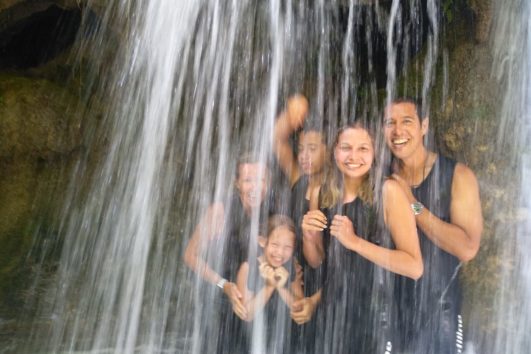 Happy family laughing as they walk through an isolated waterfall while on a rafting tour in Montenegro at the Tara river.