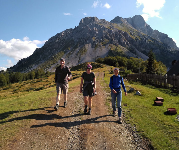 Three hikers walking away from Komovi mountain in Montenegro on a sunny day with blue sky and the odd cloud