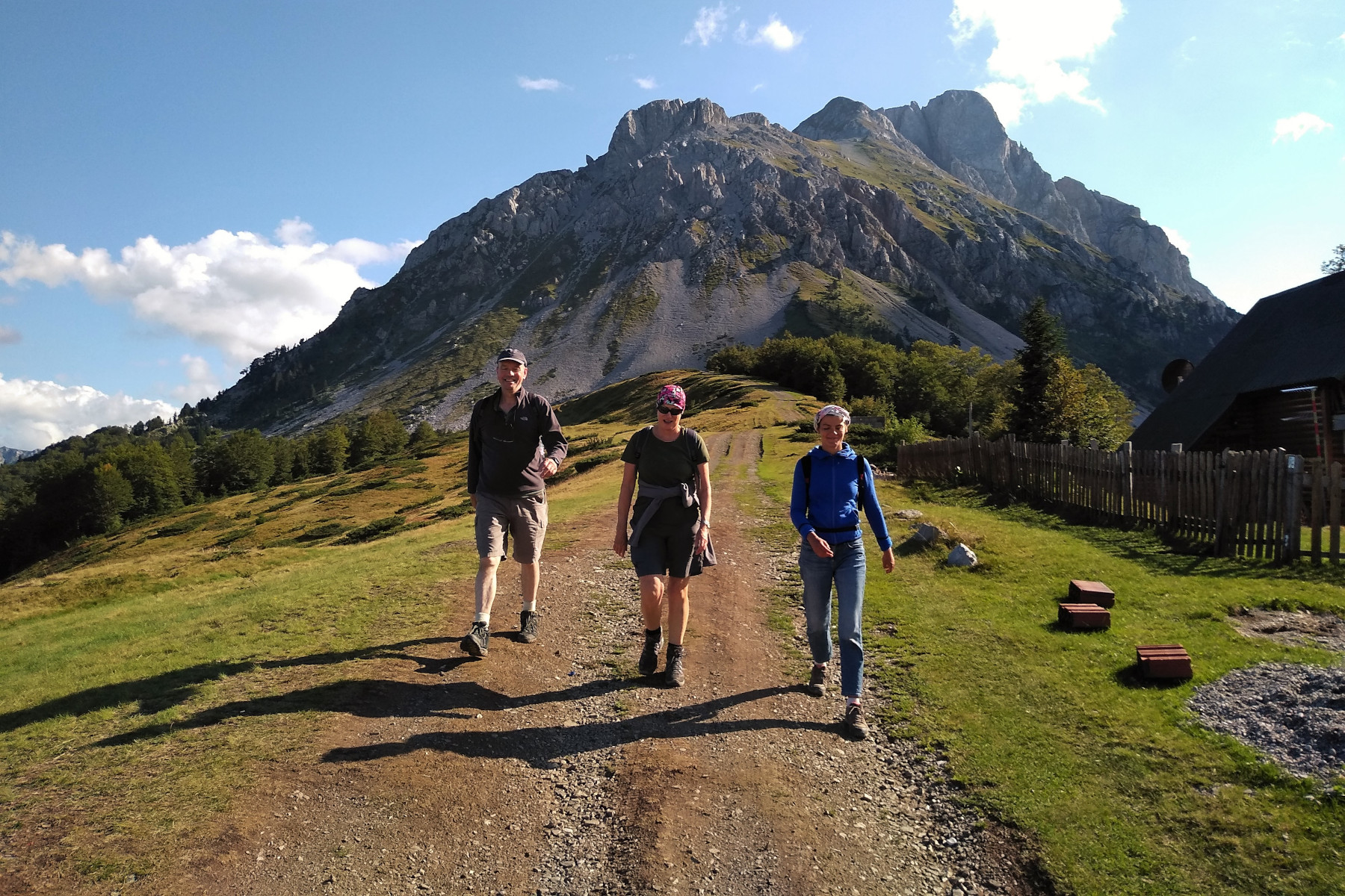 Three hikers walking away from Komovi mountain in Montenegro on a sunny day with blue sky and the odd cloud
