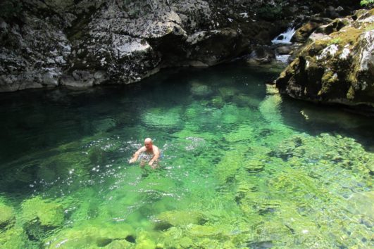 Man on an activity holiday swimming in a crystal clear, bright blue rock pool near Lake Skadar