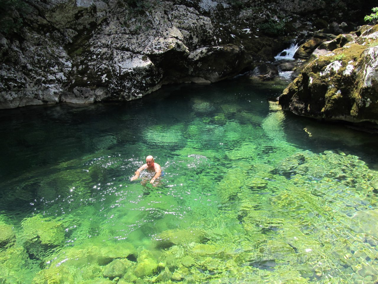 Man on an activity holiday swimming in a crystal clear, bright blue rock pool near Lake Skadar