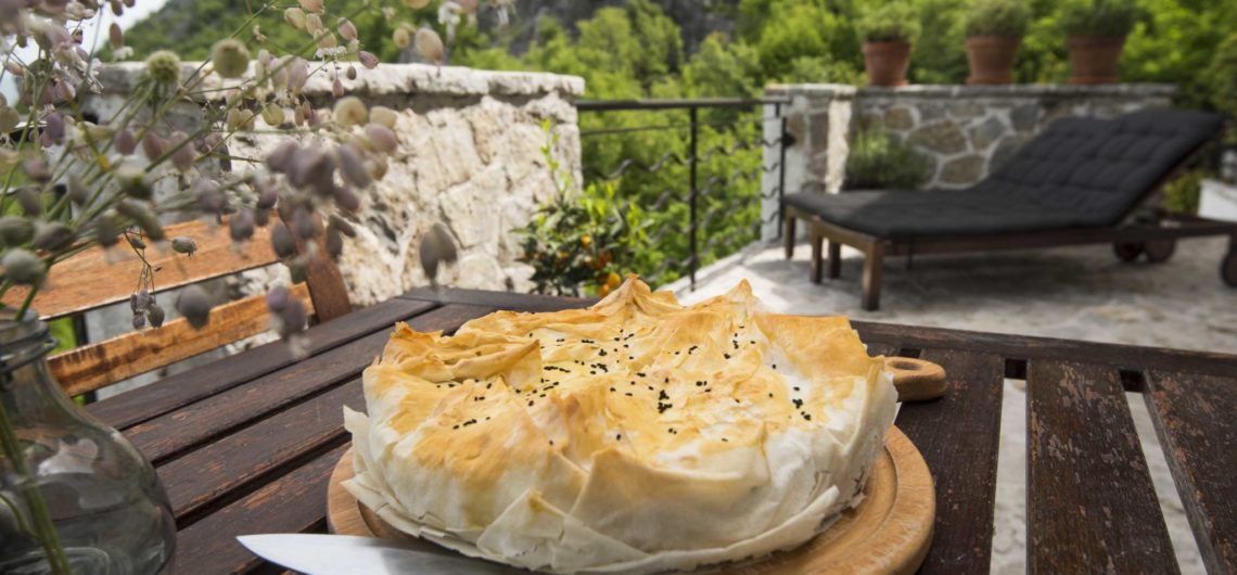A freshly baked filo pastry pie stuffed with wild greens which Montenegrins call Zelena Pita, placed on the outdoor table of Villa Miela's terrace with a backdrop of rocky mountains at Lake Skadar National Park