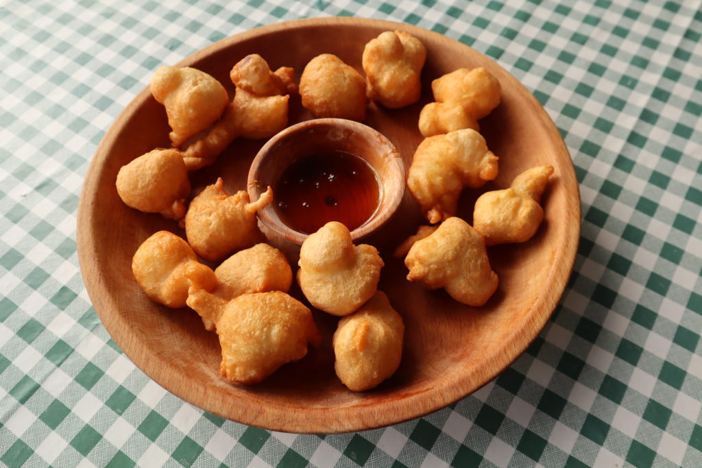 A wooden bowl full of cooked priganice dough balls placed on a table with a green and white checked tablecloth in Montenegro