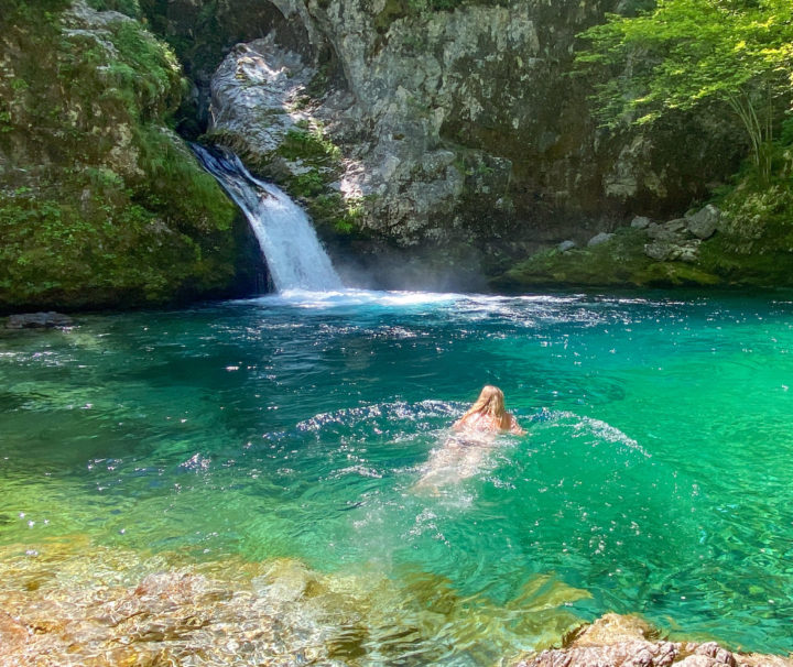 A woman swimming in a bright blue natural pool with waterfall in Albania