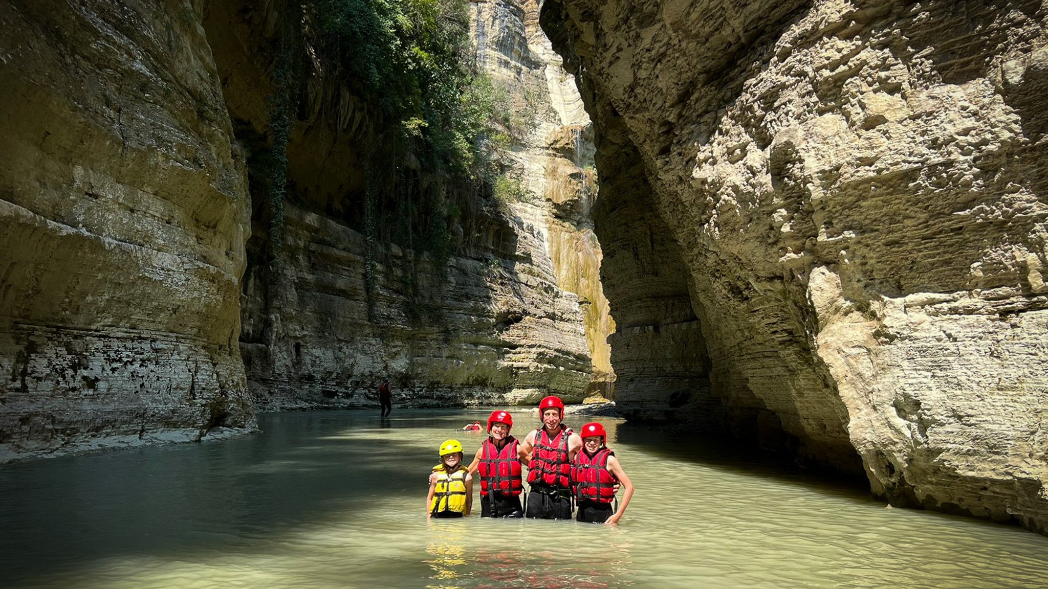 A partially-submerged family of four on a river-wading adventure at Osumi Canyon in Albania, wearing red helmets