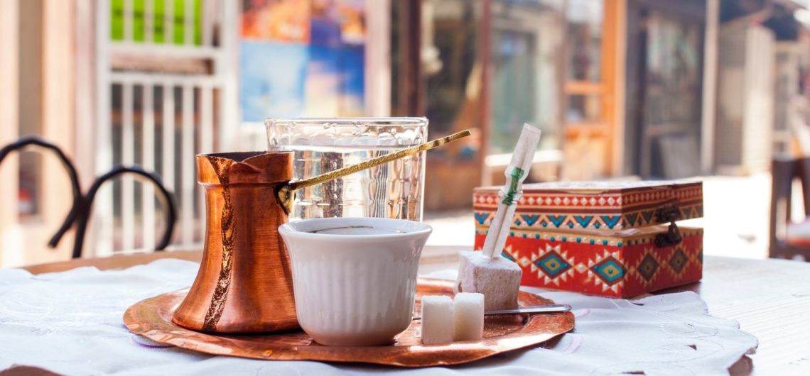 Bosnian coffee is served on a tray with a cup, glass of water, sugar cubes and rahat lokum.