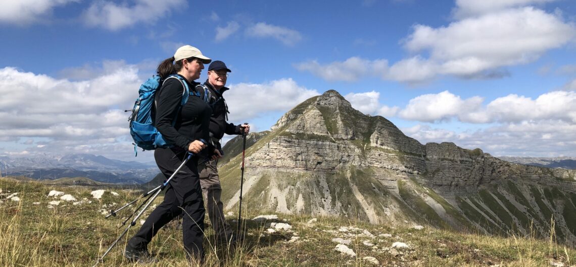 Two hikers walk with the tall rocky mountains of Montenegro's Durmitor National Park behind them