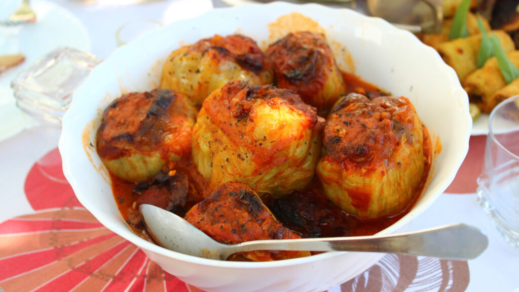 A white serving dish full of stuffed peppers with a red tomato sauce on a table in Montenegro