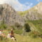 Group of hikers taking a break in a grassy valley with rugged gray rock cliffs in the background under a blue sky.