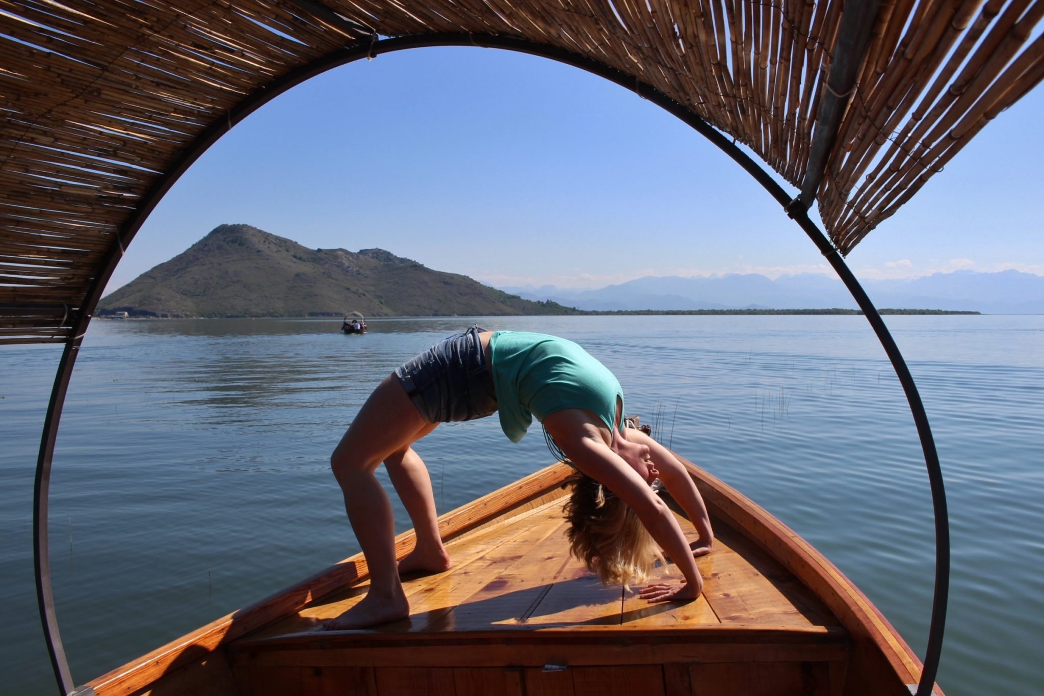 A woman on a yoga holiday in Montenegro doing a wheel pose while on a boat tour at Lake Skadar National Park on a warm sunny day